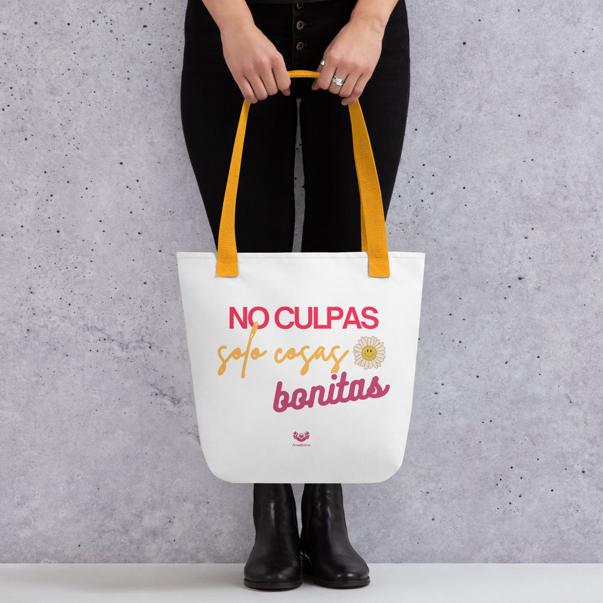 Bolsa tote “No culpas, solo cosas bonitas” con asas amarillas, vista frontal con manos sosteniéndola.