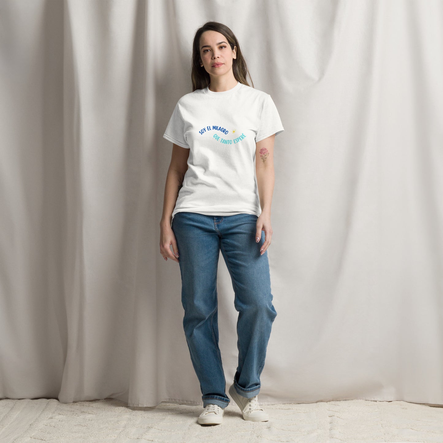 Mujer con camiseta blanca “Soy el milagro que tanto esperé” posando frente a cortina luminosa